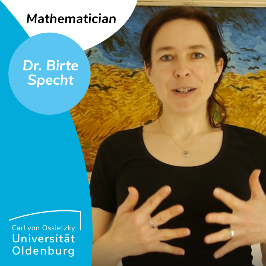 white person with dark hair (mathematician Dr. Birte Specht) standing in front of a painting, wearing a black t-shirt, a silver necklace and two silver rings. She is weraring her hair in a ponytail and is gesturing with her hands while speeking, seemingly giving a lecture. 

